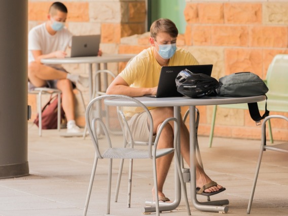 UA Students wearing masks outside while on their laptops 