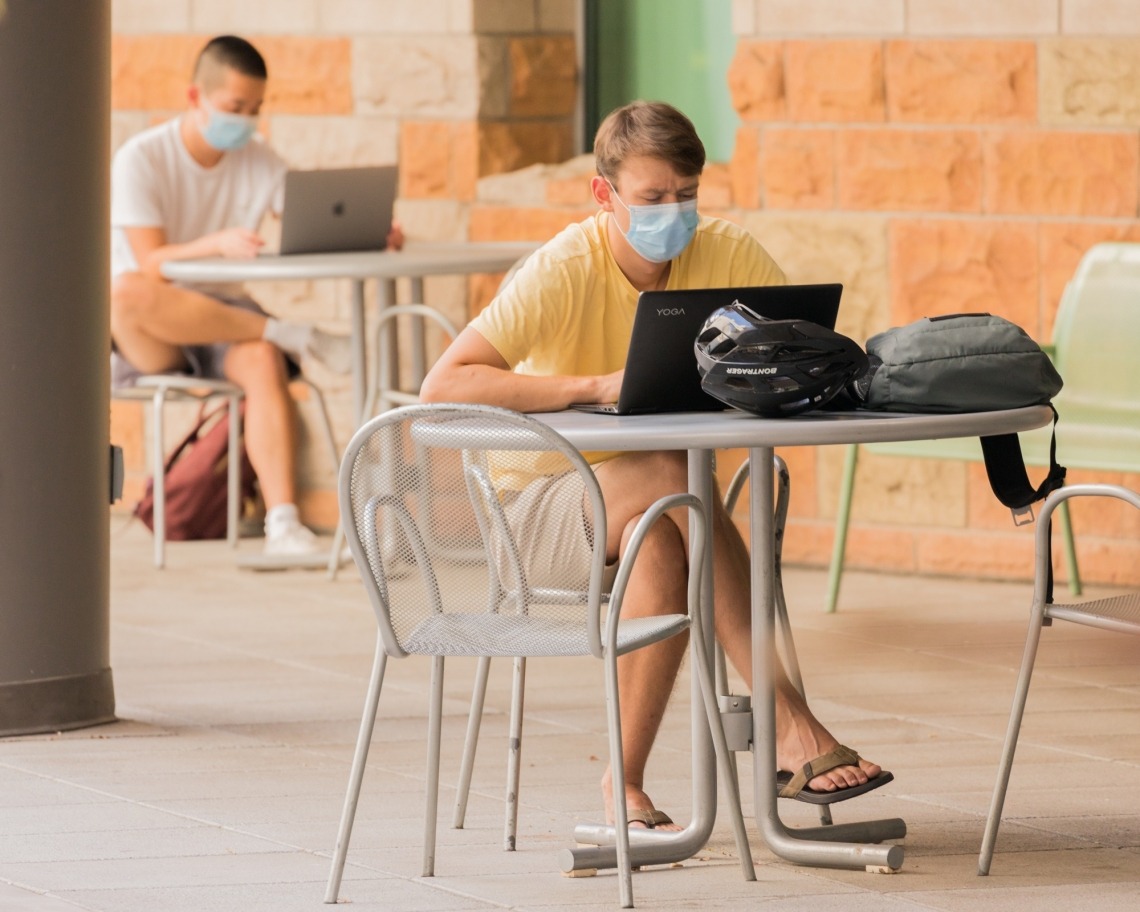UA Students wearing masks outside while on their laptops 